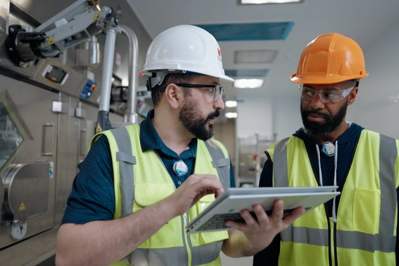 Two employees in hard hats talking in a manufacturing facility 