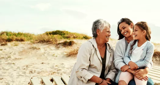 Grandmother, mother and daughter smiling and laughing on a beach