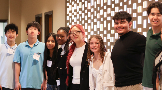 Group of students standing indoors wearing name tags in front of a patterned wall